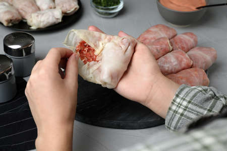 Woman making stuffed cabbage rolls at gray table, closeup