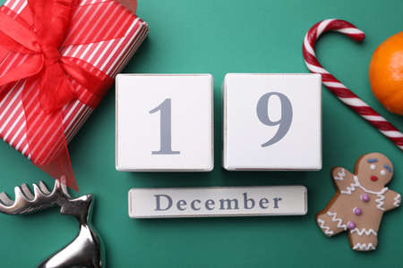 Wooden block calendar with date 19th of December, gift box, treats and festive decor on green background, flat lay. Saint Nicholas Dayの写真素材