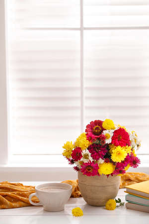 Cup of fresh coffee, books and beautiful bouquet on white wooden table near window. Good morningの写真素材