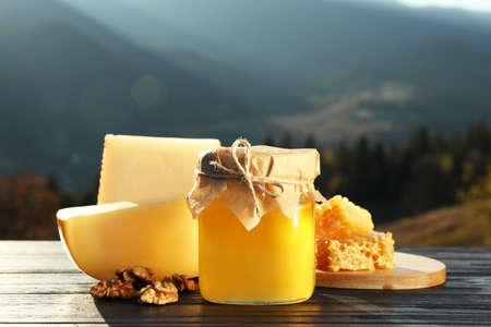 Fresh aromatic honey, combs, cheese and nuts on wooden table against mountain landscapeの写真素材