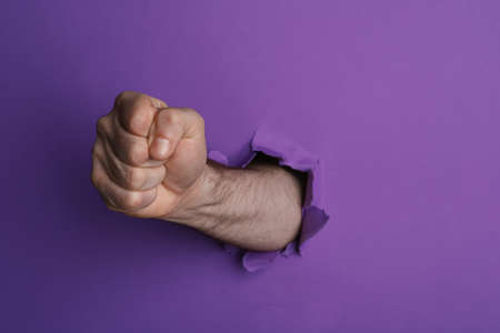 Man breaking through purple paper with fist, closeupの写真素材