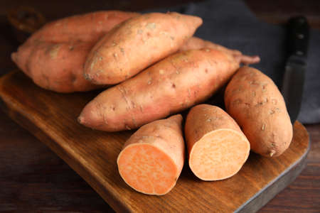 Whole and cut ripe sweet potatoes on wooden board, closeupの写真素材