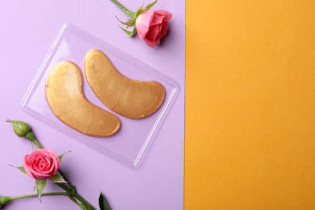 Under eye patches and rose flowers on color background, flat lay with space for text. Cosmetic productの写真素材