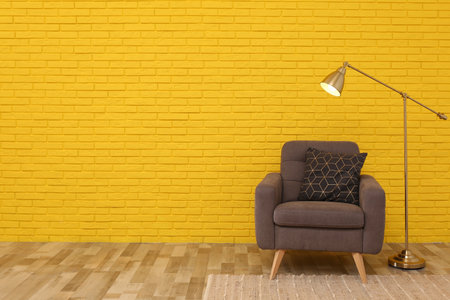 Stylish armchair and lamp near yellow brick wall in room, space for text. Interior designの写真素材