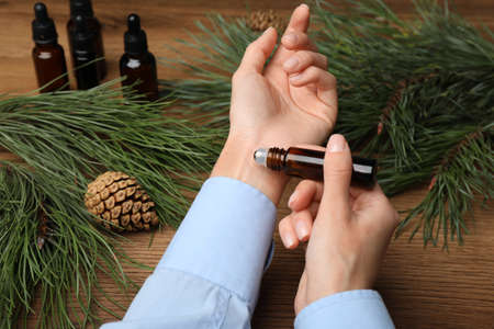 Woman applying pine essential oil on wrist at wooden table, closeupの写真素材