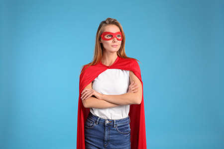 Confident woman wearing superhero cape and mask on light blue backgroundの写真素材