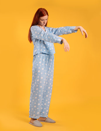 Young woman wearing pajamas and slippers in sleepwalking state on yellow backgroundの写真素材
