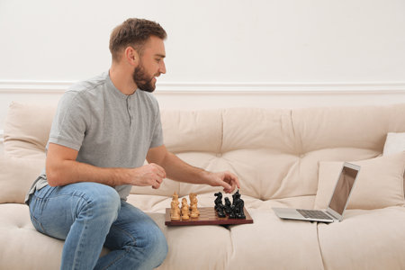 Young man playing chess with partner through online video chat at home