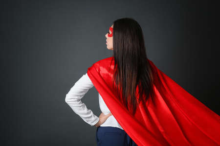 Confident businesswoman wearing superhero cape and mask on gray background, back viewの写真素材