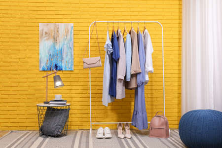 Rack with different stylish clothes and shoes near yellow brick wall in roomの写真素材