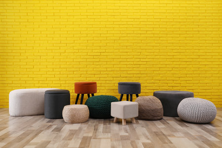Different stylish poufs and ottomans near yellow brick wall, space for textの写真素材