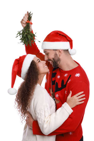 Lovely couple in Santa hats under mistletoe bunch on white backgroundの写真素材