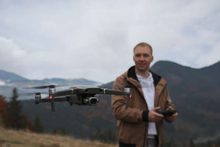 Young man operating modern drone with remote control in mountains