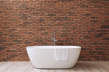 Modern ceramic bathtub with towel near brick wallの写真素材
