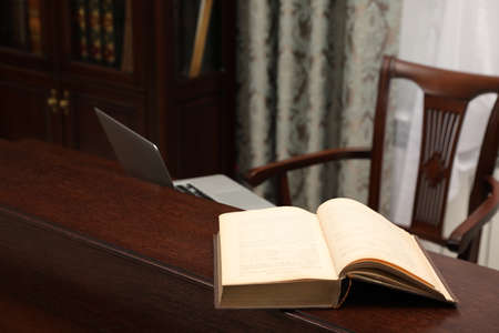 Old book and laptop on wooden table in library reading room
