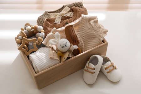 Wooden crate with children's clothes, toys and pacifier near shoes on white table in roomの写真素材