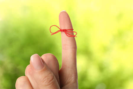 Woman showing index finger with tied red bow as reminder on blurred green background, closeupの写真素材