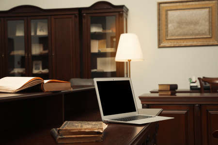 Old books and laptop on wooden table in library reading roomの写真素材