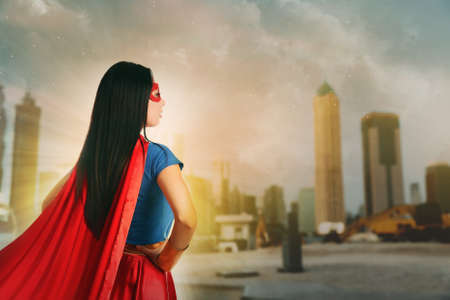 Confident young woman wearing superhero costume and beautiful cityscape on backgroundの写真素材