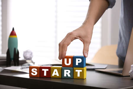 Woman forming words Start Up with colorful cubes at table in office, closeup. Space for textの写真素材