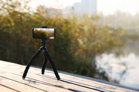 Tripod with smartphone on wooden pier near riverの写真素材