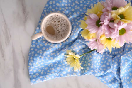Cup of fresh coffee and beautiful bouquet on light blue printed cloth, top view. Good morning