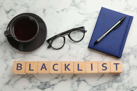 Wooden cubes with word Blacklist, cup of coffee and office stationery on white marble table, flat layの写真素材