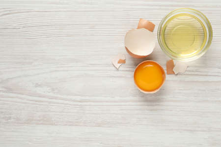 Yolk in broken chicken eggshell and bowl with white on wooden table, flat lay. Space for text