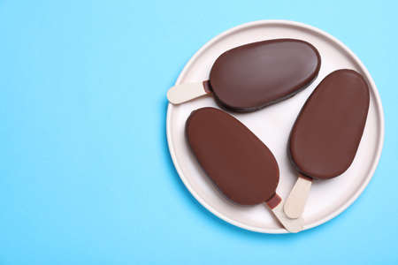 Plate with glazed ice cream bars on light blue background, top view. Space for textの写真素材