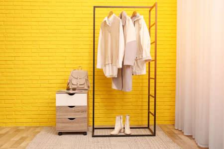 Rack with stylish clothes near yellow brick wall indoorsの写真素材