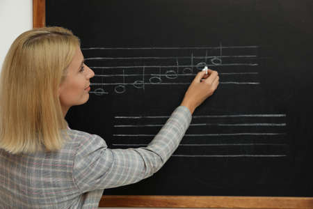 Teacher writing music notes with chalk on blackboard in classroomの写真素材