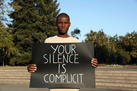African American man holding sign with phrase Your Silence Is Complicit outdoors. Racism conceptの写真素材
