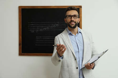Teacher near black chalkboard with music notes in classroomの写真素材