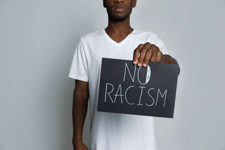 African American man holding sign with phrase No Racism on gray background, closeup