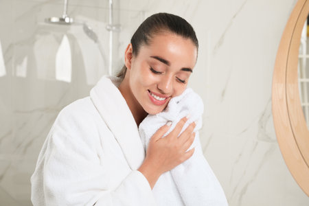 Beautiful young woman wiping face with towel in bathroom. Facial washの写真素材