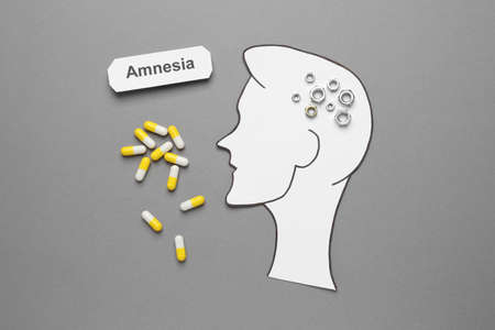 Word Amnesia, pills and human head cutout with metal nuts as brain on gray background, flat layの写真素材