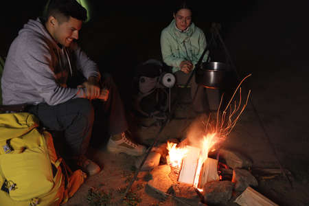 Couple sitting near bonfire in camp at night