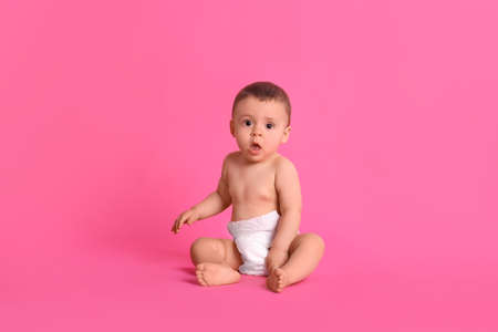 Cute baby in dry soft diaper sitting on pink backgroundの写真素材