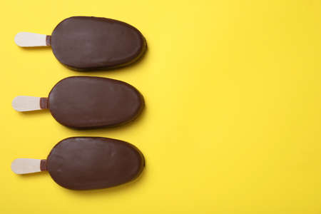 Glazed ice cream bars on yellow background, flat lay. Space for textの写真素材