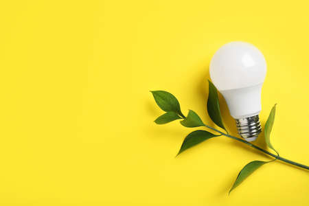 Light bulb and branch with green leaves on yellow background, flat lay. Space for text