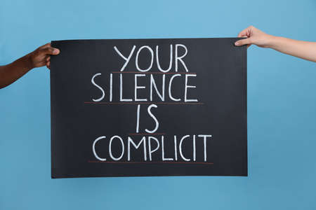 Woman and African American man holding sign with phrase Your Silence Is Complicit on light blue background, closeup. Racism conceptの写真素材