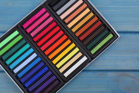 Set of colorful pastels in box on light blue wooden table, top view. Drawing materialsの写真素材