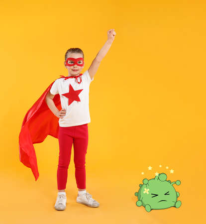 Little girl wearing superhero costume won in fight against virus on yellow backgroundの写真素材