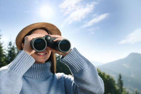 Young woman with binoculars in mountains on sunny dayの写真素材