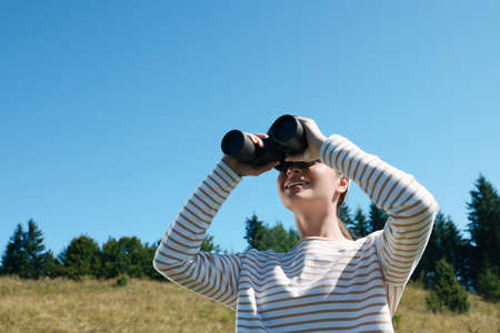 Woman looking through binoculars outdoors on sunny dayの写真素材