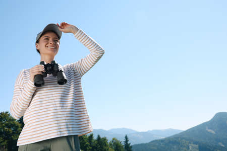 Woman with binoculars in mountains on sunny day, low angle viewの写真素材