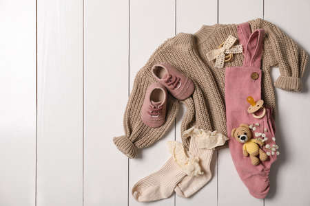 Flat lay composition with children's clothes, shoes and toy on white wooden table. Space for text
