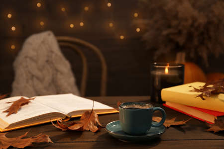 Cup of aromatic coffee, books and autumn leaves on wooden table indoors. Space for textの写真素材