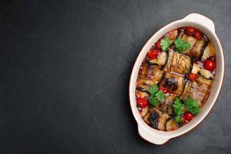 Tasty eggplant rolls with tomatoes, cheese and parsley in baking dish on black table, top view. Space for textの写真素材
