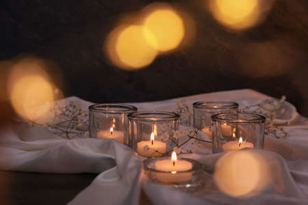 Burning candles and flowers on table against blurred festive lightsの写真素材